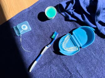 Zahnpflegeset auf einem blauen Handtuch: Zahnbürste, Zahnseide, Mundspülung und transparente Zahnschiene in einem blauen Aufbewahrungsbehälter – dargestellt im Sonnenlicht.
