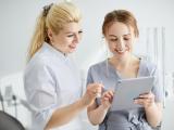 Zwei Zahnärztinnen in heller Praxiskleidung schauen gemeinsam auf ein Tablet und besprechen etwas – moderne digitale Praxisorganisation.