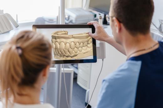 Zahnarzt zeigt einer Patientin ein digitales 3D-Modell eines Gebisses auf einem Bildschirm in der Praxis