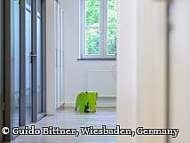 Moderner, heller Flur einer Praxis mit großem Fenster und einem grünen Kinderspiel-Elefanten aus Kunststoff im Hintergrund.