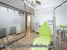 Moderner Behandlungsraum in einer Zahnarztpraxis mit grünem Behandlungsstuhl, Glaswänden und heller, freundlicher Einrichtung.