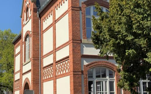 Außenansicht eines historischen Backsteingebäudes mit dekorativen Fassadenelementen und großen Fenstern